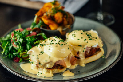 Enjoy a plate of eggs Benedict with hollandaise sauce, served alongside mixed greens and roasted potatoes at our Nashville Mother's Day Brunch 2026.