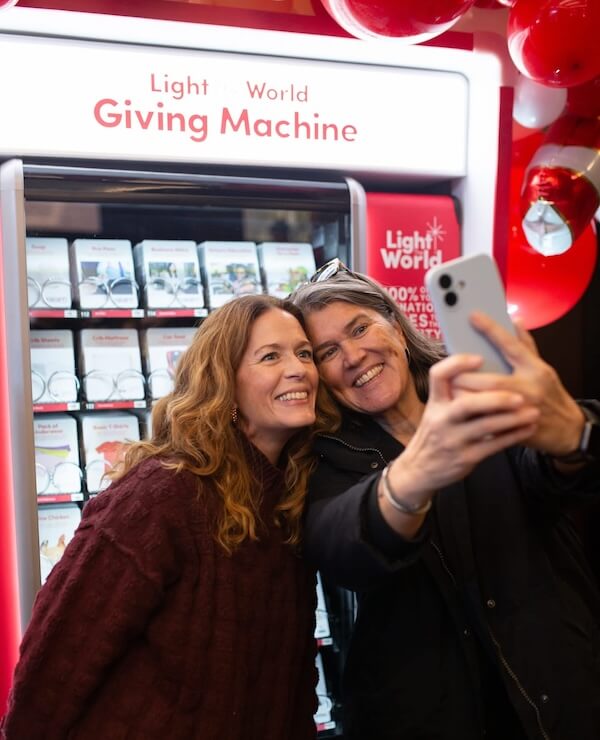 It Started with a StyleBlueprint Story — Now This Nashville Nonprofit Is Turning 10! - 2 Two women smile and take a selfie in front of a “Giving Machine” vending display, highlighting Nashville community connections, with red and white balloons visible in the background.