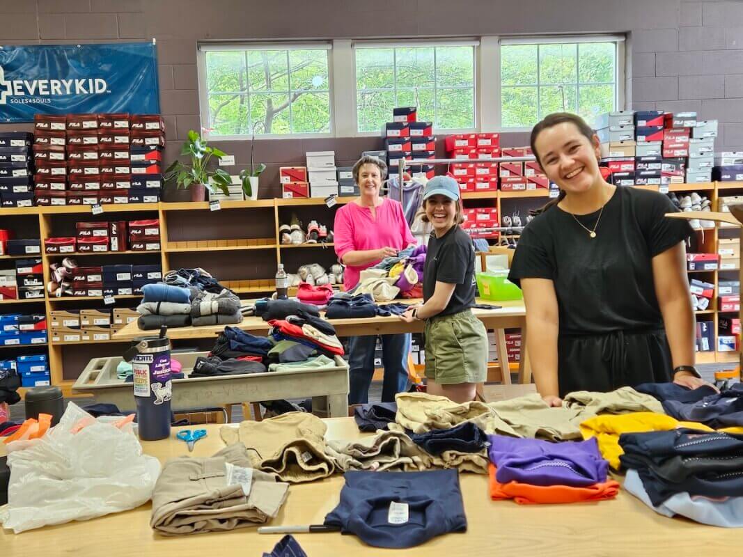 Three people sort and fold clothes on tables in a room filled with shelves of shoes and windows, reflecting the spirit of Nashville community connections.