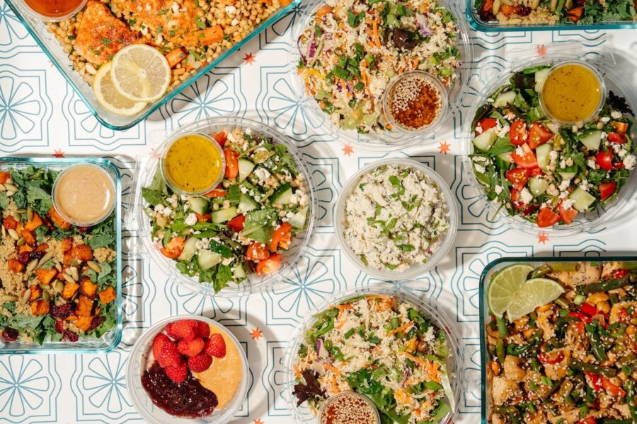 An assortment of salads, grains, and vegetables in bowls and trays, with dressings and small sides, arranged on a patterned table—perfect inspiration for April 2026 menus at new Nashville restaurants.