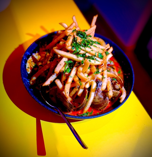 A bowl of mussels in red sauce topped with French fries and chopped herbs, served with a spoon on a yellow table—a must-try dish at one of the top Nashville restaurants opening in April 2026.