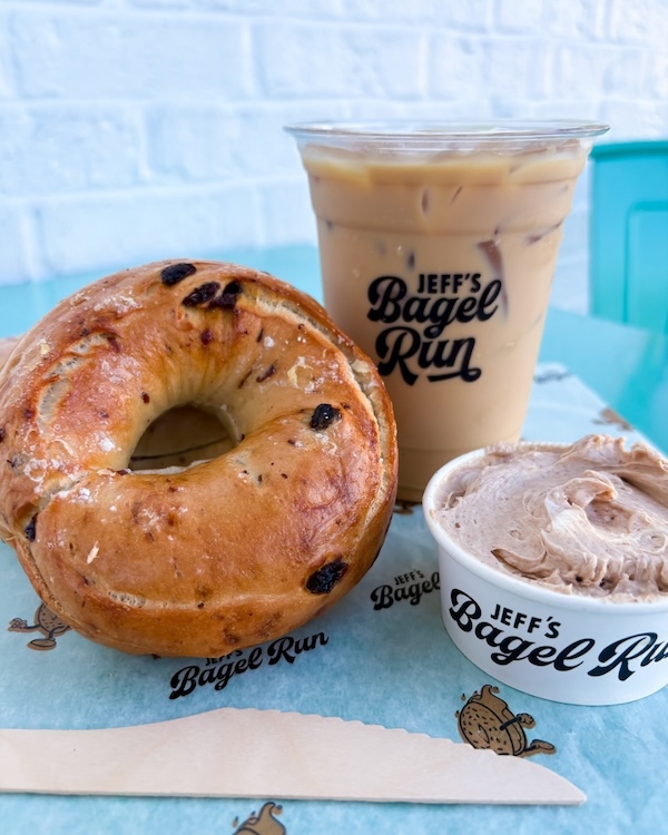 A cinnamon raisin bagel, a cup of iced coffee, and a container of spread on branded paper from Jeff's Bagel Run—one of the exciting new Nashville restaurants set to shine in April 2026.