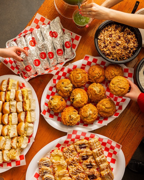 A variety of breakfast foods including muffins, pastries, sandwiches, wrapped burritos, and a bowl of granola are arranged on a wooden table—perfect inspiration for new restaurants opening in Nashville in April 2026.