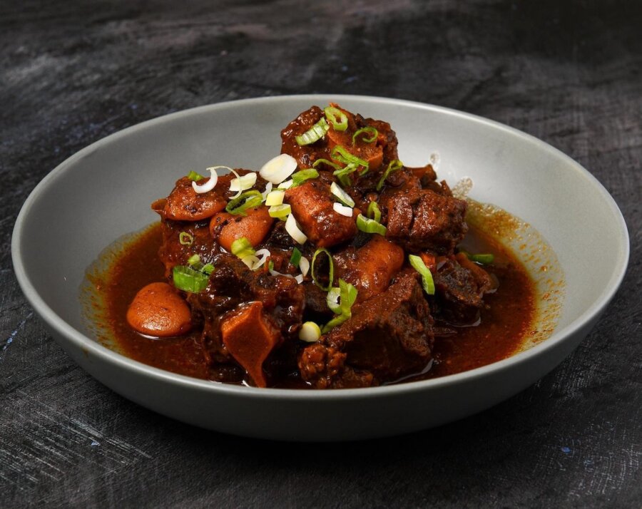A bowl of braised meat stew with carrots and potatoes in a rich brown sauce, topped with chopped green onions—a comforting dish inspired by new restaurants opening in Nashville.