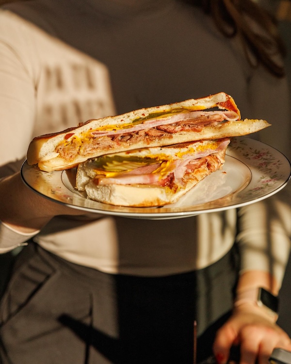 A person holding a plate with two halves of a sandwich filled with meat, cheese, and mustard, ready to sample the flavors inspired by new Nashville restaurants opening in April 2026.