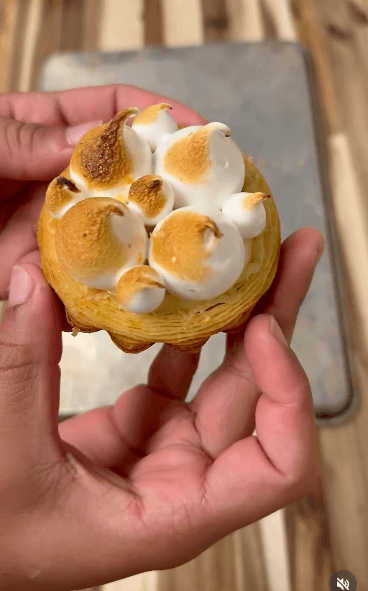 7 New Nashville Restaurants to Try This Month - 5 A hand holds a round pastry topped with toasted dollops of meringue, reminiscent of the inventive desserts found at new Nashville restaurants, with a baking tray in the background.