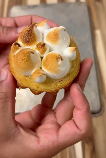 11 New Nashville Restaurants to Try This Month - 8 A person holds a small pastry topped with browned meringue peaks, reminiscent of the creative desserts found at new Nashville restaurants, with a metal tray and wooden surface in the background.