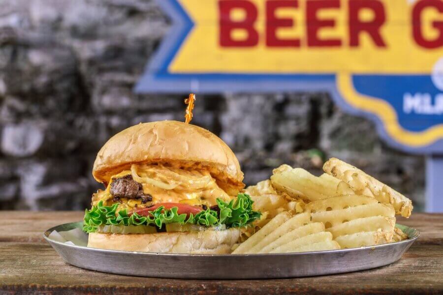 10 Nashville Smashburgers Worth the Hype - 3 A Nashville smashburger with lettuce, tomato, and onions served on a metal tray with a side of crinkle-cut fries.