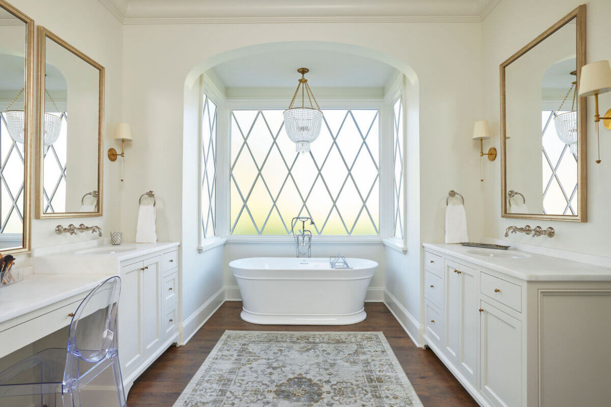 Shea Bryars on lntentional Interior Design β and Saying No to 'Amazon Living Rooms' - 13 A bright bathroom with a freestanding bathtub under a chandelier, flanked by two vanities, large mirrors, and diamond-patterned windows.
