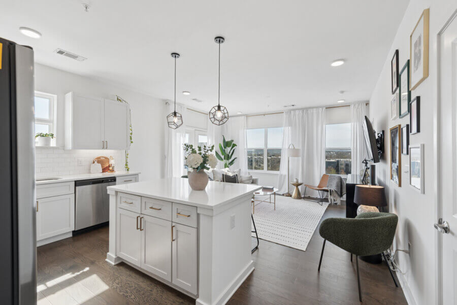Modern open-concept kitchen and living room at 1677 54th Ave N, featuring white cabinets, island with drawers, pendant lights, large windows, and neutral-toned furnishings—perfect for Nashville real estate seekers.