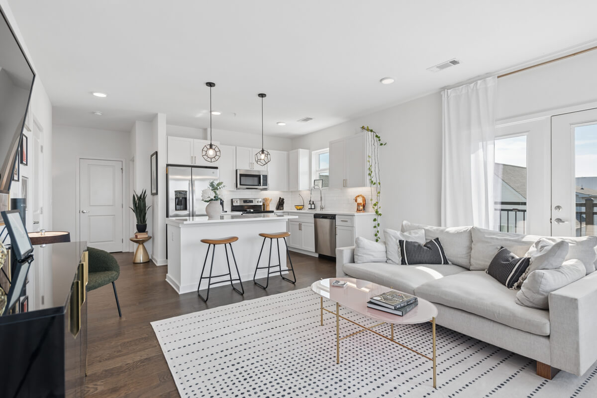 Modern open-concept living room and kitchen at 1677 54th Ave N, Nashville, with white cabinetry, island seating, gray sofa, coffee table, and large windows letting in natural light.