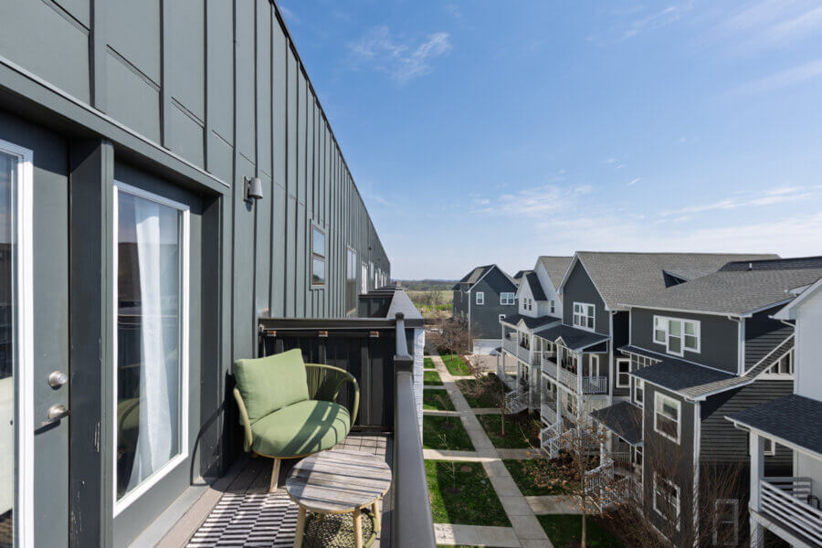 View from a balcony with green chair and small table, overlooking a row of modern gray townhouses and a sidewalk on a clear Nashville day at 1677 54th Ave N.