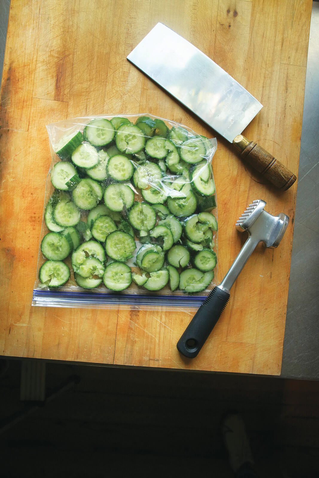 3 Cool, Crisp Recipes from the 'Down South + East' Cookbook - 4 A cutting board with cucumbers in a plastic bag, and a knife and mallet by its side.
