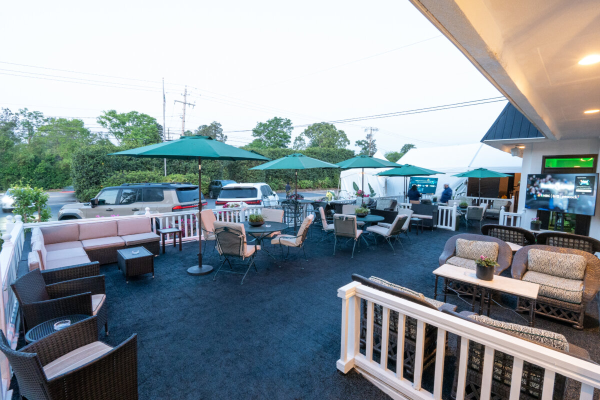 A Masters-Inspired Design Project You Need to See - 3 Outdoor patio with cushioned seating, tables, and green umbrellas. Several cars and trees are visible in the background, evoking a Masters Tournament vibe.