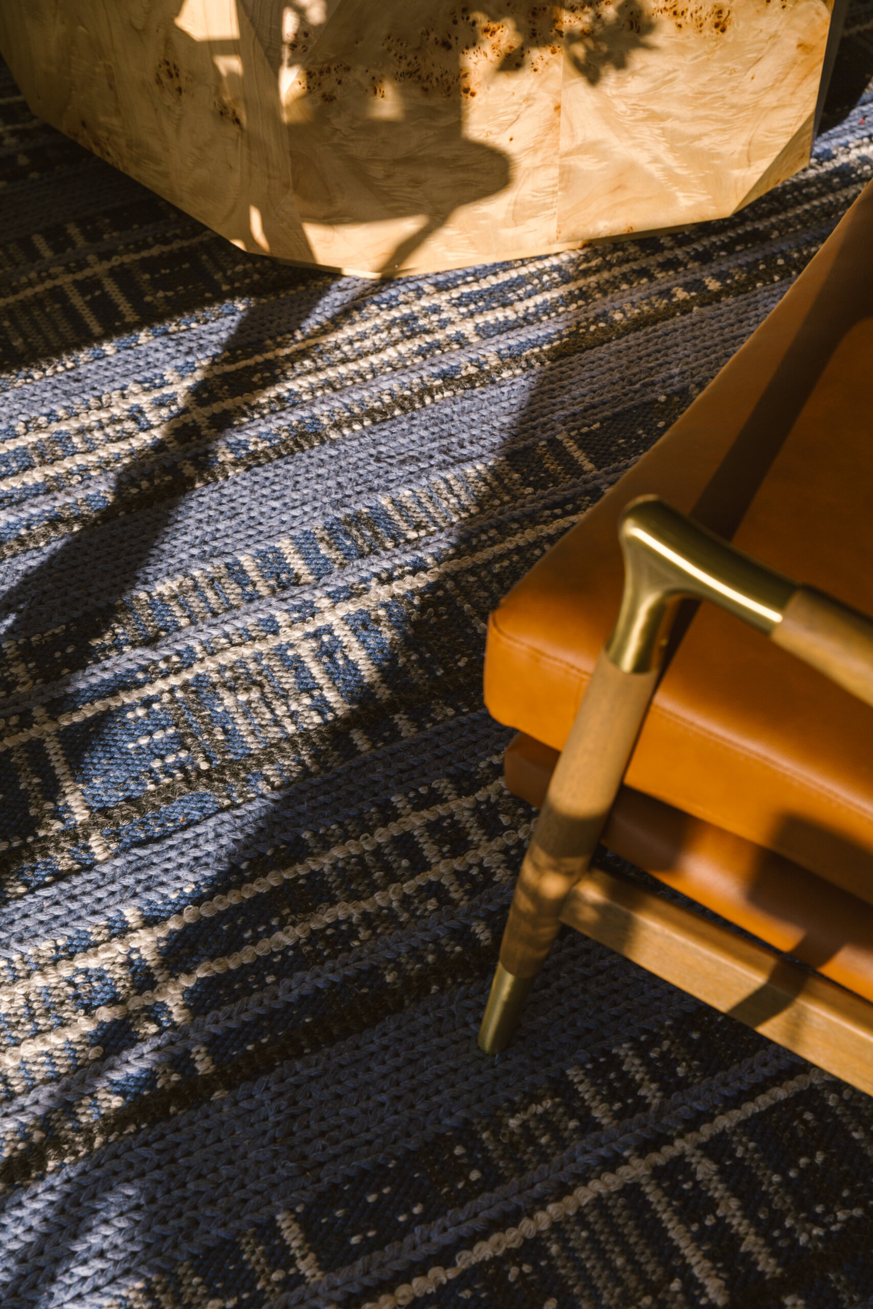 A Masters-Inspired Design Project You Need to See - 8 Sunlight casts shadows on a blue plaid patterned rug next to a tan leather chair with wooden and brass armrests.