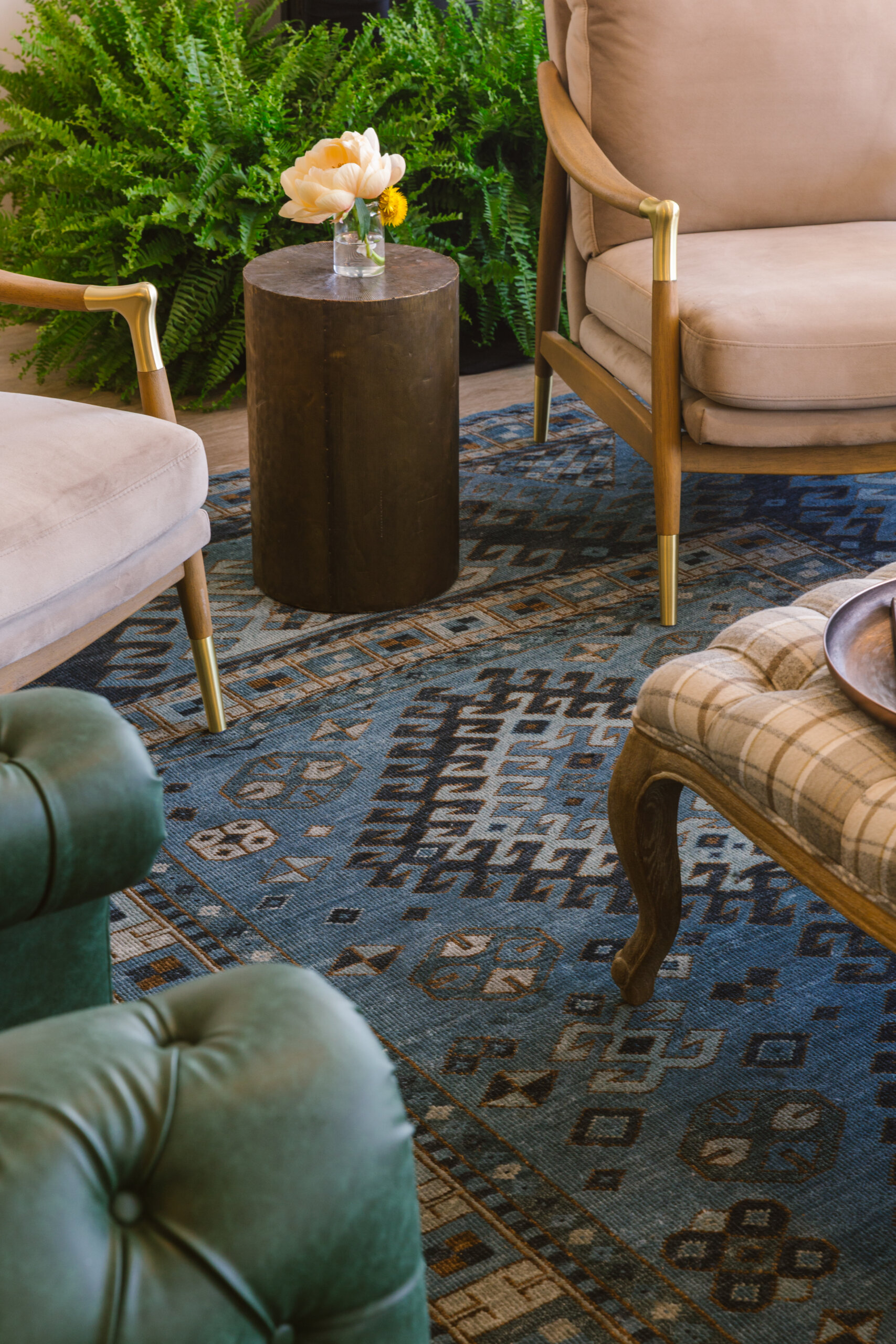 A Masters-Inspired Design Project You Need to See - 10 A seating area with upholstered chairs, a small round wooden table holding a glass vase with flowers, and a patterned blue rug, with green ferns in the background.