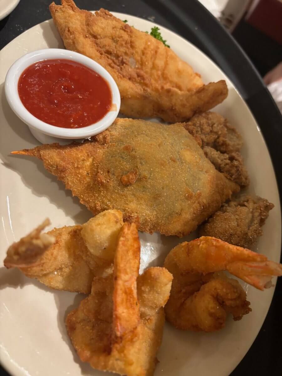 The South's Oldest Restaurants, Still Operating Today - 2 A plate with assorted fried seafood—shrimp, fish, and oysters—served with cocktail sauce.