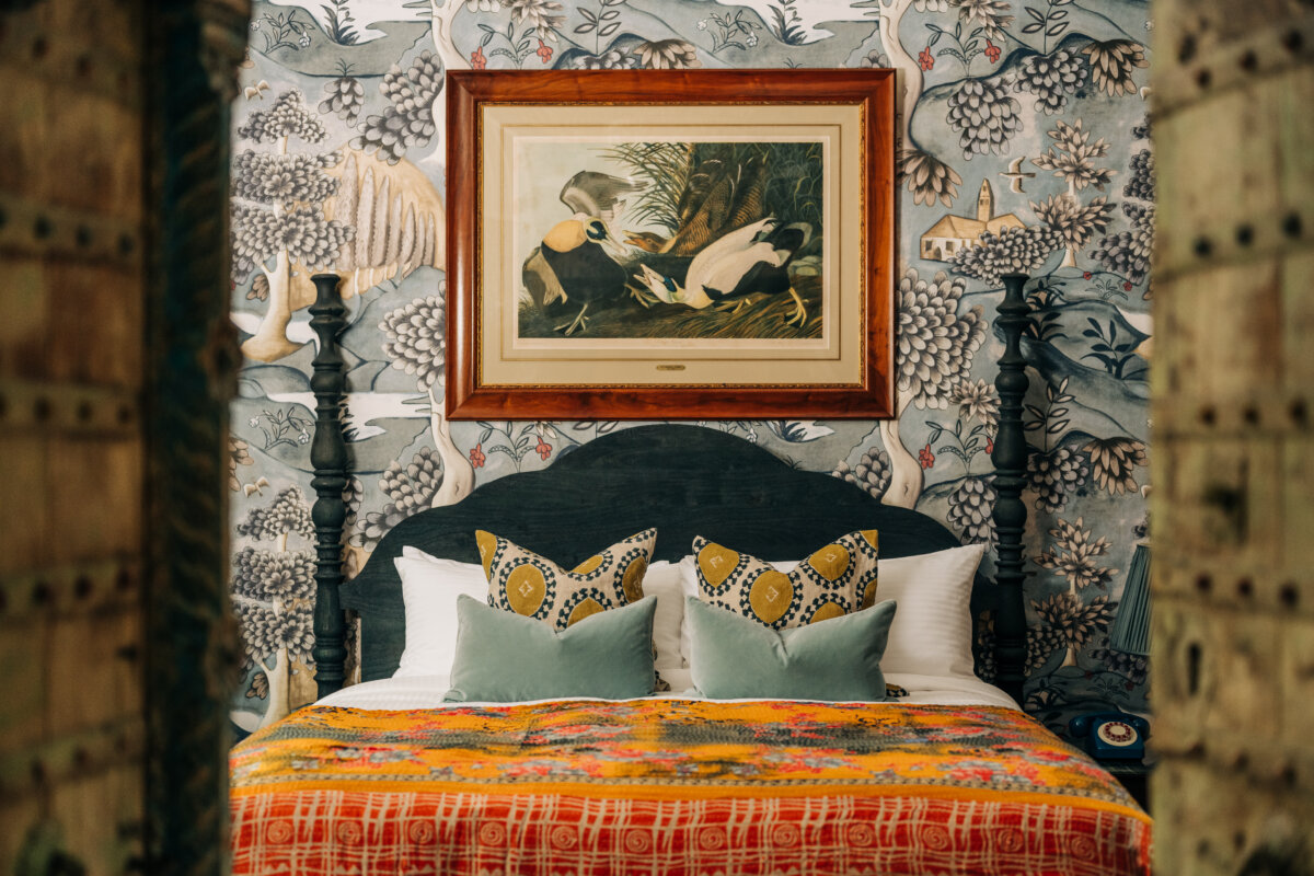 She's Behind Camp Lucy, a Dreamy Austin-Area Escape - 8 An ornately wallpapered guest bedroom with patterned decorative pillows and a colorful bedspread.