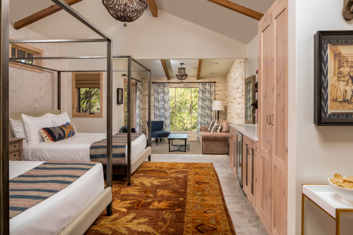 She's Behind Camp Lucy, a Dreamy Austin-Area Escape - 5 A spacious bedroom at Camp Lucy features two canopy beds, an area rug, a sitting area with a couch and chair, large windows, wooden ceiling beams, and built-in cabinets.