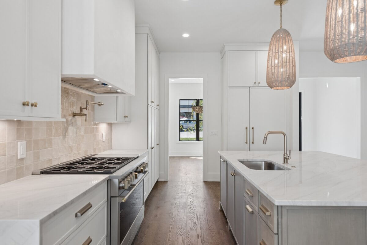 Modern kitchen at 508 Stonewall Way with white cabinets, marble countertops, a gas stove, built-in oven, center island with sink, and two woven pendant lights in desirable Brentwood, TN.