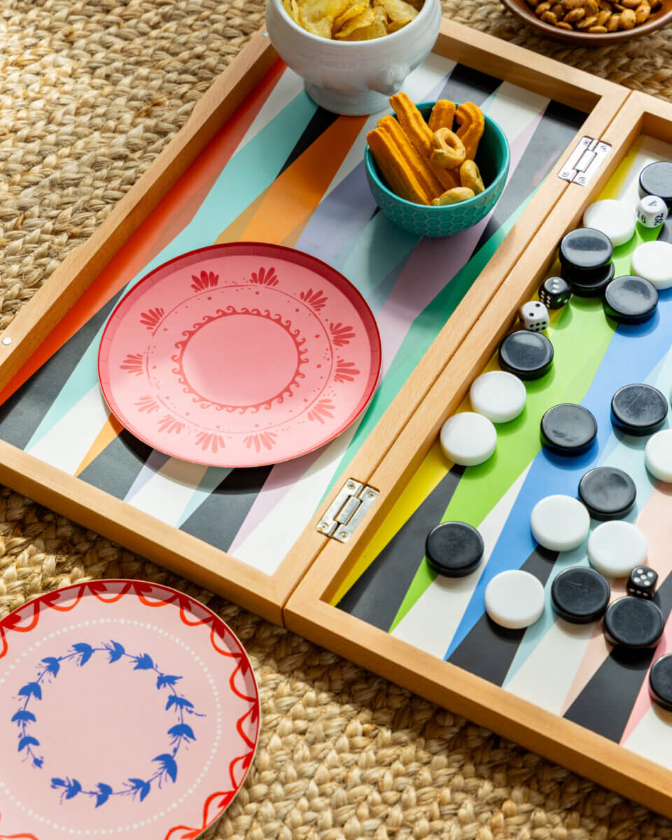 Table Two Studio's Luxe Paper Plates Will Change How You Entertain - 11 A backgammon board with black and white pieces, luxury paper plates by Table Two Studio, and bowls of snacks on a woven mat.