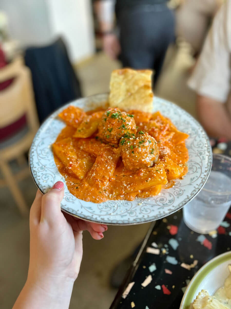 4 Summer Weekend Trips from Atlanta - 3 A hand holding a plate with rigatoni pasta in red sauce, two meatballs, and a piece of bread—perfect comfort food.