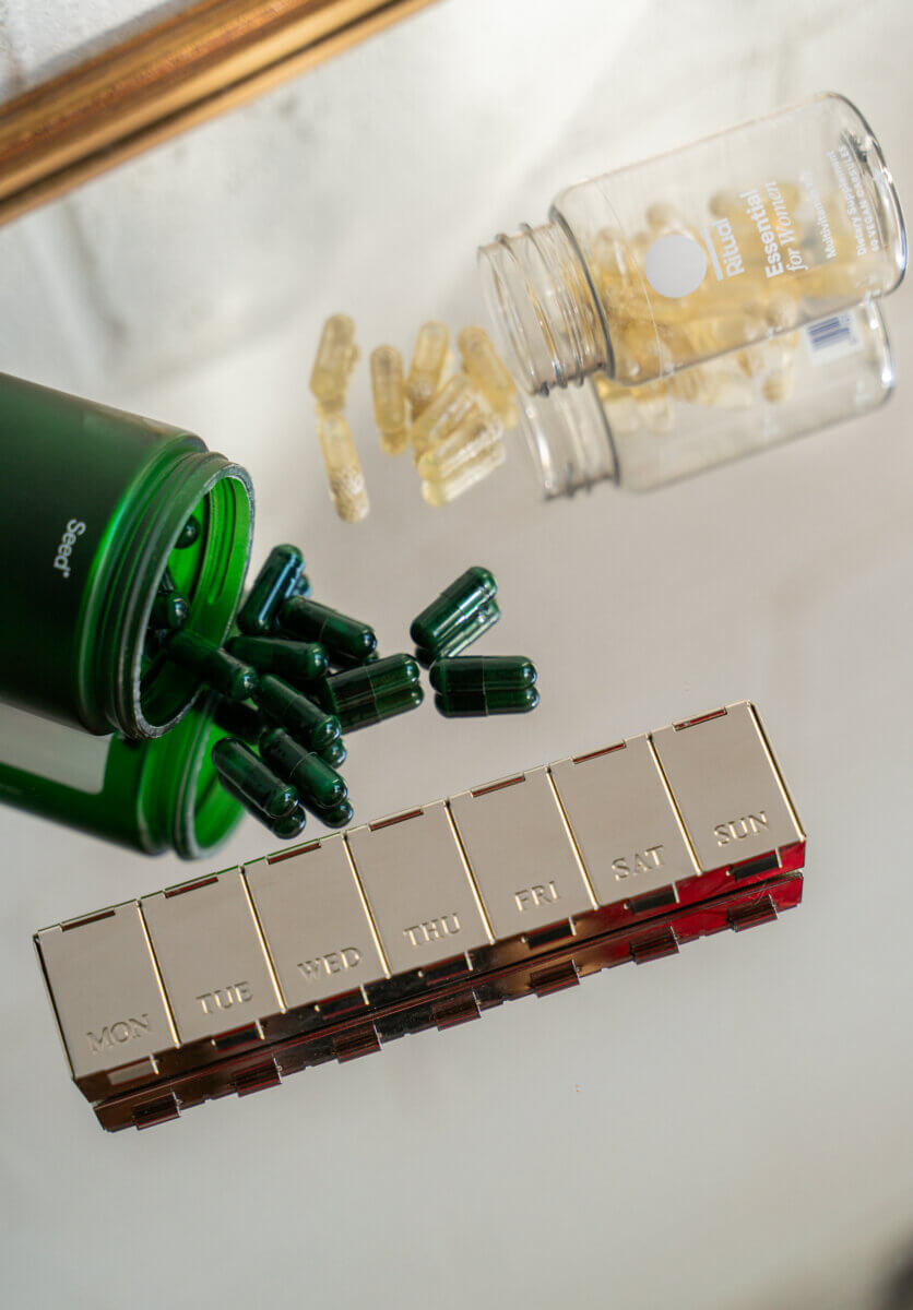 Is It Time for Hormone Therapy? What You Need to Know - 5 Two pill bottles on a mirror, with pills spilling out, next to a gold case for daily pills.