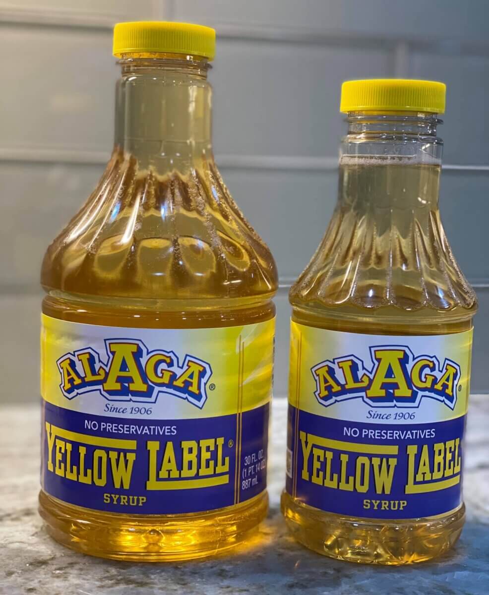 ALAGA Syrup: Alabama's IYKYK Staple - 5 Two bottles of ALAGA Syrup, an Alabama staple, one large and one small, are placed side by side on a countertop.