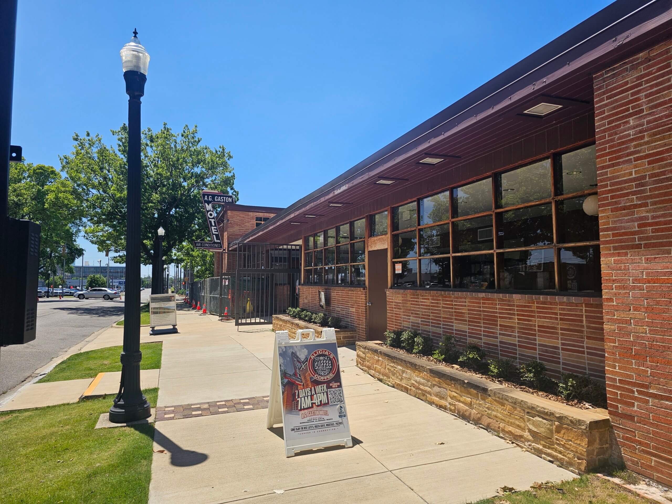 A sidewalk runs alongside a brick building with large windows and a sign advertising an event on the pavement. A vintage motel sign and lamp post are visible.