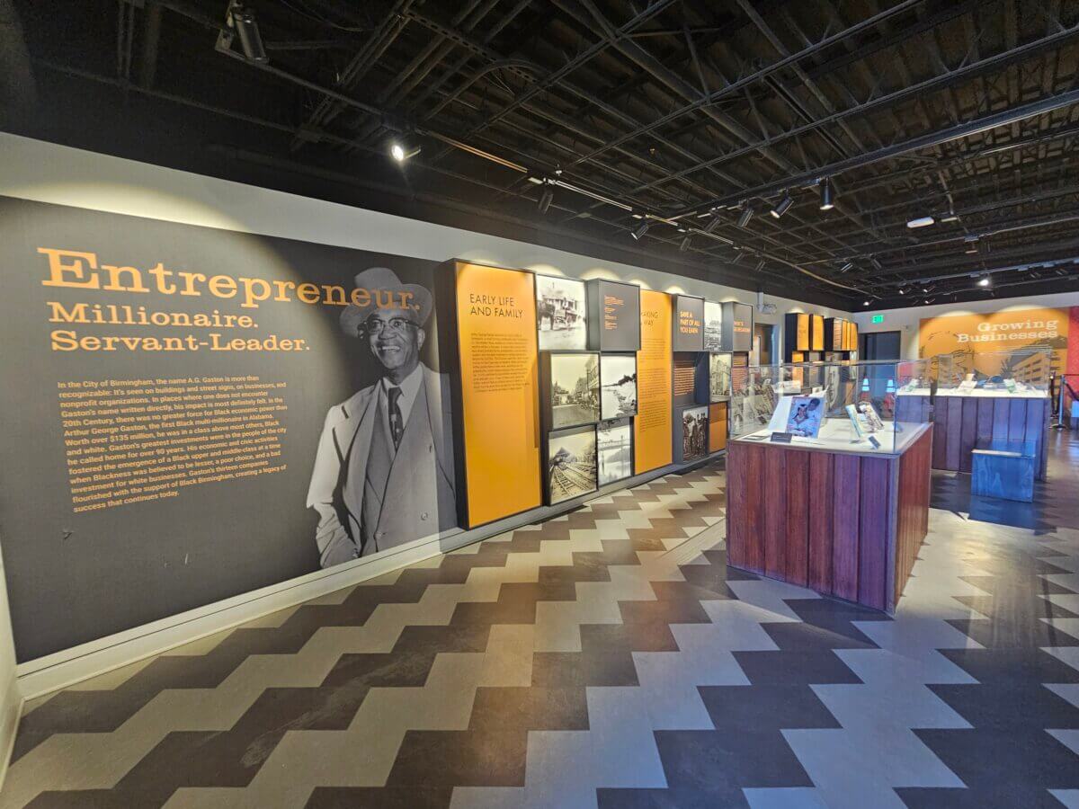 How Two BHAM Creatives Built a Coffee Shop Centered on Connection - 5 The A.G. Gaston exhibit features a large wall display about an entrepreneur, with photos and text panels, plus display cases on a zigzag-patterned floor.