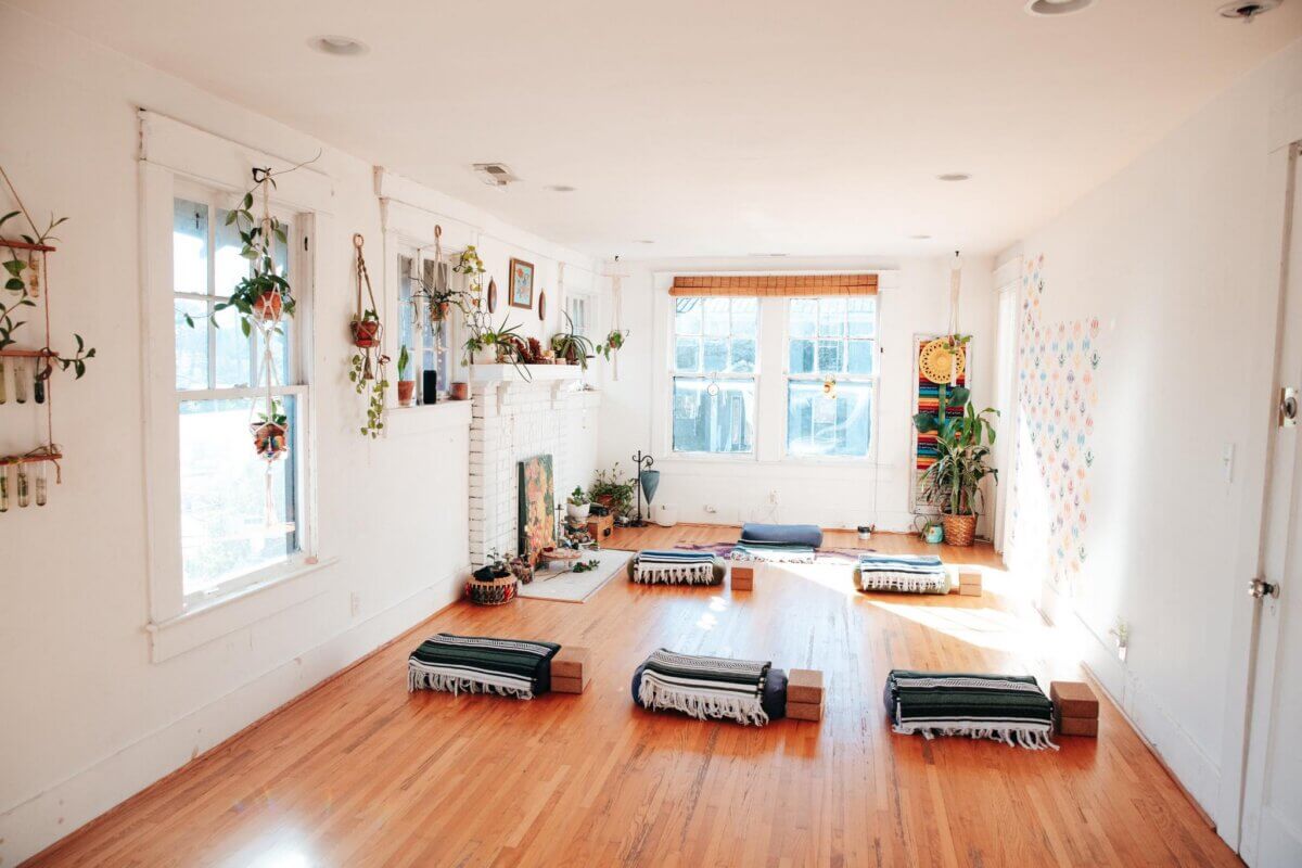 Your Guide to BHAM's Forest Park Neighborhood - 5 A bright yoga studio in Forest Park with hardwood floors, six yoga mats with blankets and blocks, lush potted plants, and sunlight streaming through large front windows.