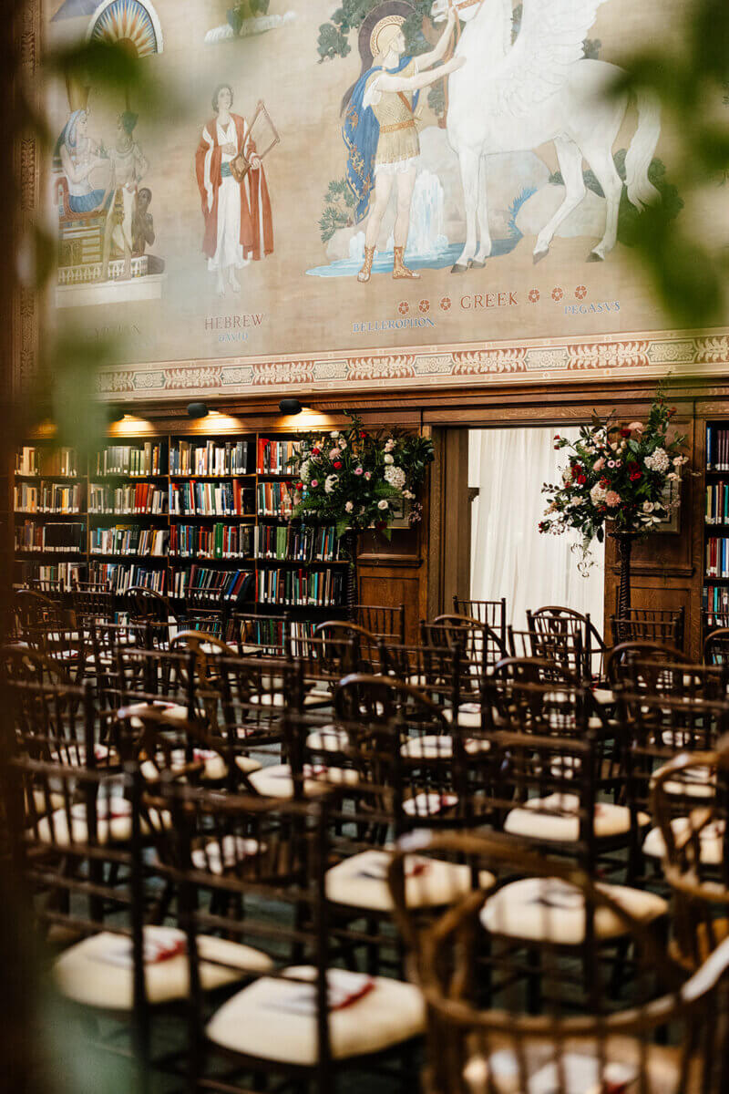 Rows of empty chairs face a decorated wall in the Linn-Henley Research Library, with bookshelves and a grand mural above—an enchanting setting perfect for a storybook wedding.