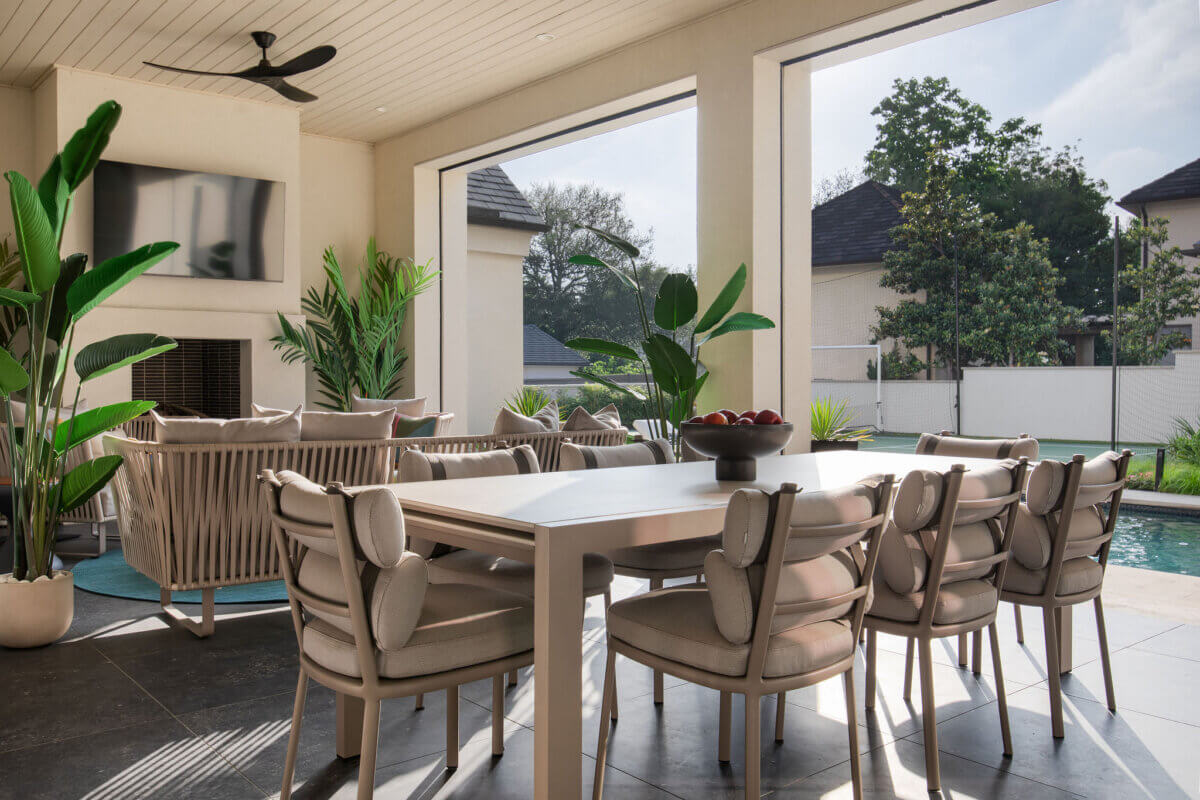 This Dallas Home Masters the Art of Quiet Luxury - 18 Modern Dallas home outdoor patio with a dining table and chairs, lounge seating, potted plants, ceiling fan, wall-mounted TV, and a view of the pool.