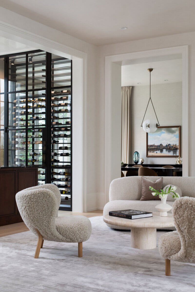 This Dallas Home Masters the Art of Quiet Luxury - 4 Modern living room with two cream boucle chairs, a round coffee table, and a glass wine storage area; perfect for an NYC family looking to move South and enjoy the comfort of a modern Dallas home.