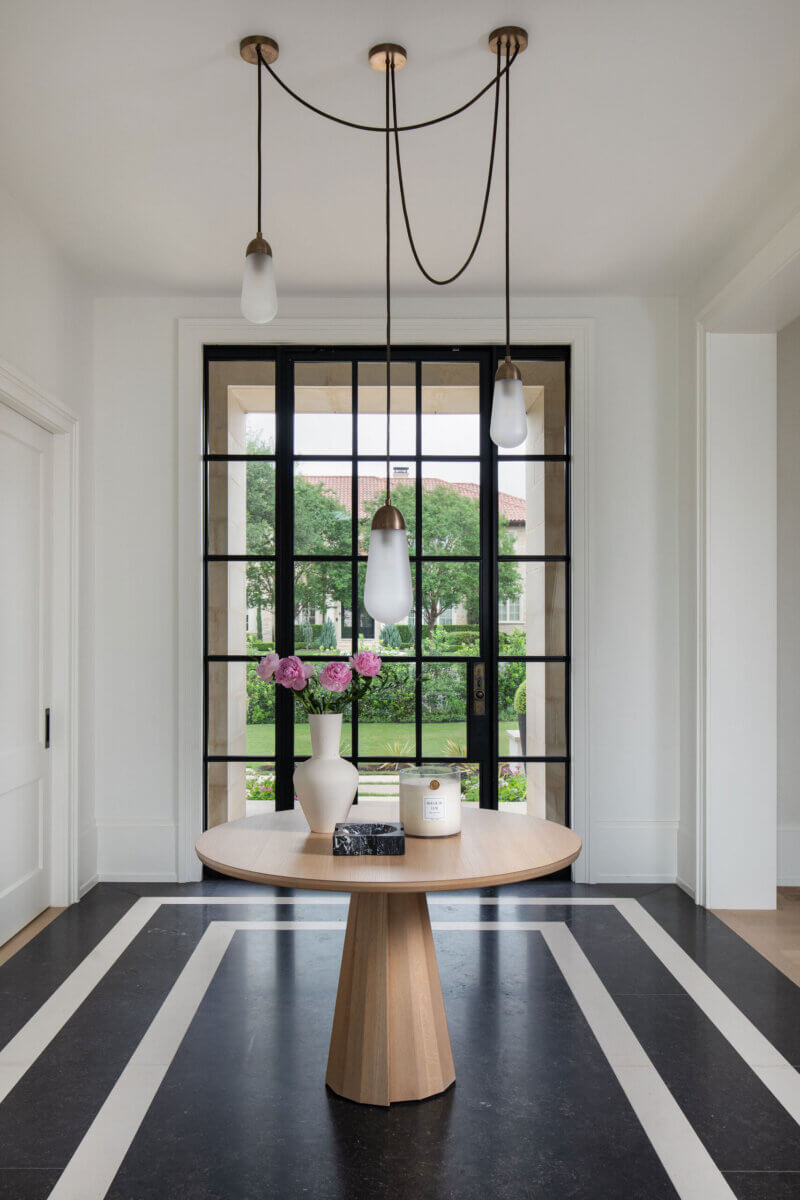 This Dallas Home Masters the Art of Quiet Luxury - 12 A round wooden table with a white vase of pink flowers and candles sits under three pendant lights in the entryway of a modern Dallas home, welcoming an NYC family after their move South.