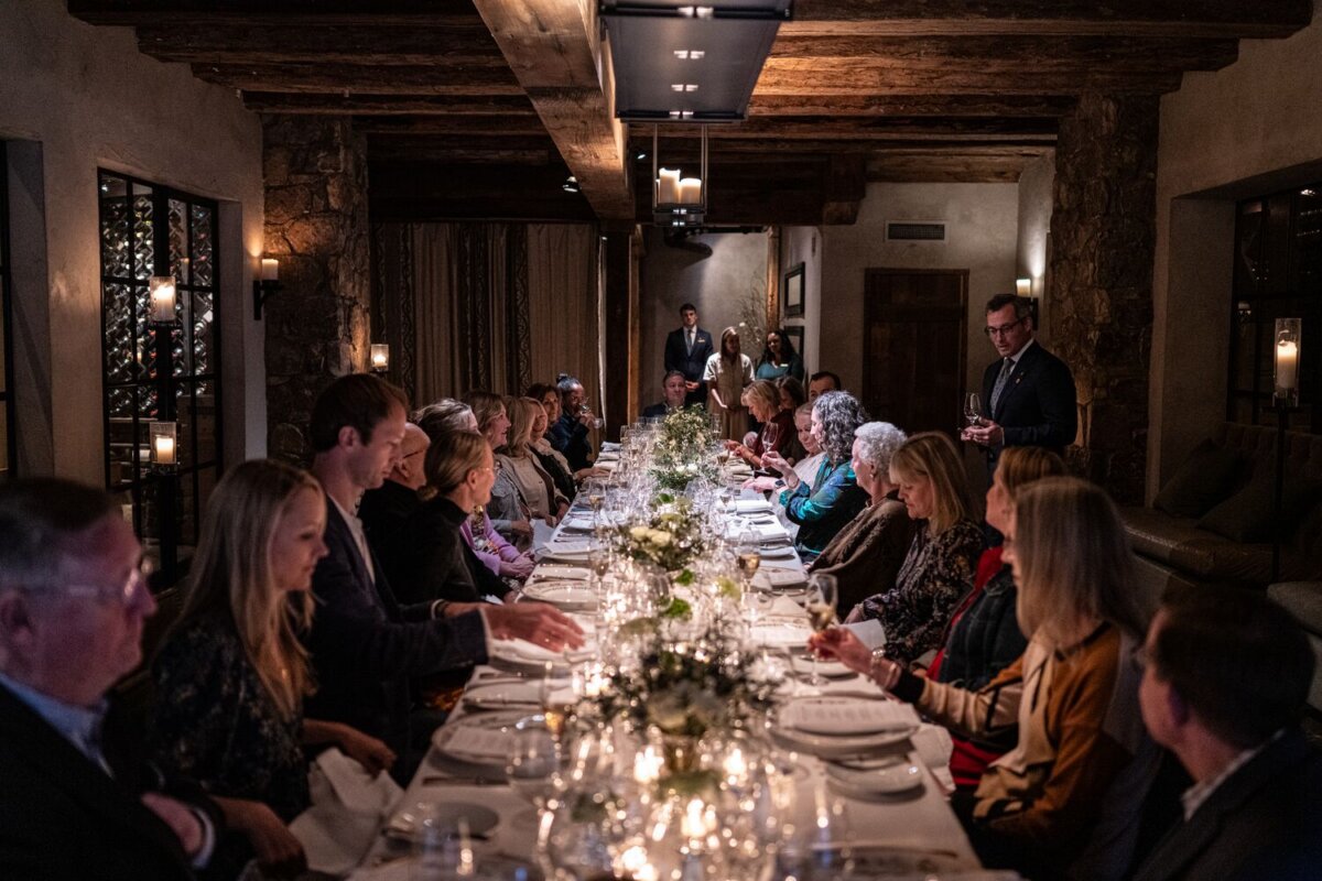 Meet the Woman Behind Tennessee's Beloved Blackberry Farm - 5 A group of people sit around a long, elegant dinner table in a dimly lit room at Blackberry Farm, engaged in conversation, with floral centerpieces and candles on the table.