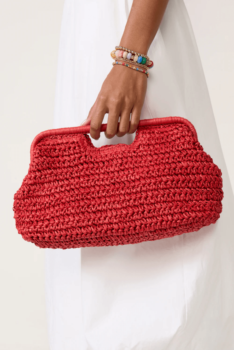 A person wearing a white dress and colorful beaded bracelets holds a large red woven handbag with a handle—perfect for Candy Crush vibes and bold, colorful bags this season.