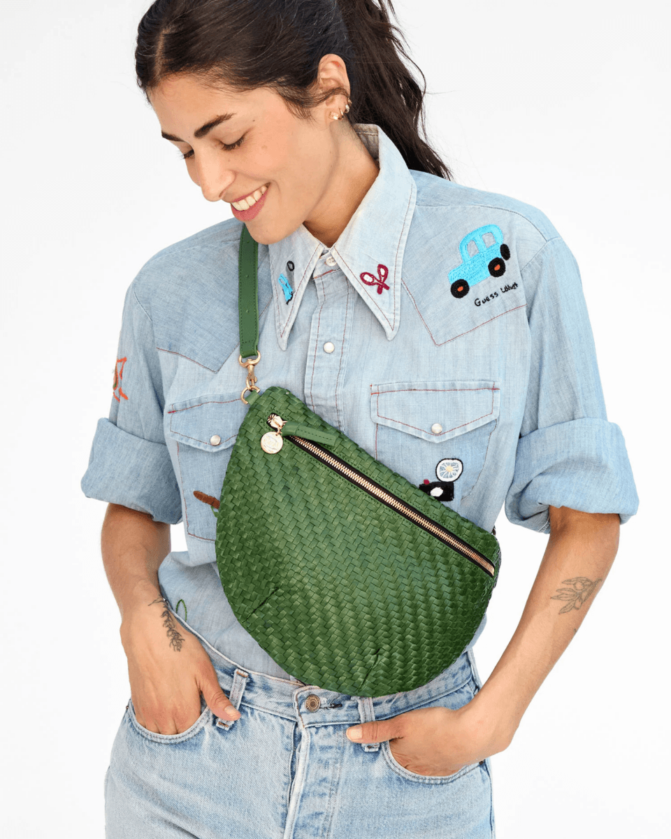 A woman wearing a light denim shirt with patches smiles while carrying one of this season’s colorful bags—a vibrant green woven crossbody.