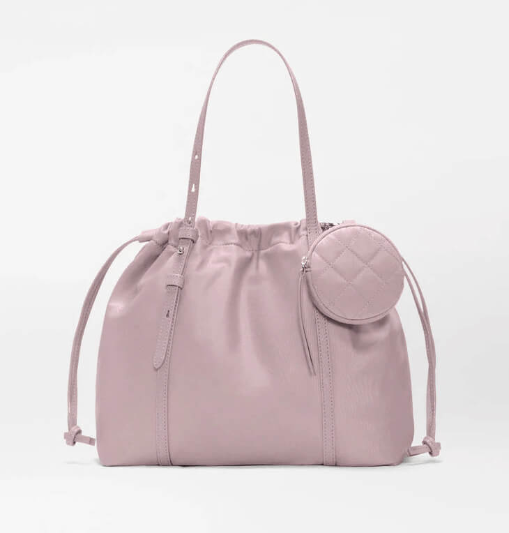 A light mauve drawstring tote bag with double handles and a round quilted coin pouch attached, perfect for those who love colorful bags with practical details.