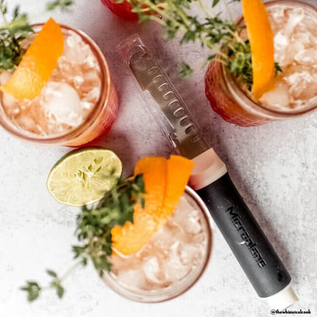20 Nashville FINDS for June: Father's Day Gifts, Chic Accessories & More - 20 Three iced cocktails garnished with orange peel and herbs, a halved lime, and a metal zester on a light surface—perfect for savoring Nashville’s finest FINDS this May.