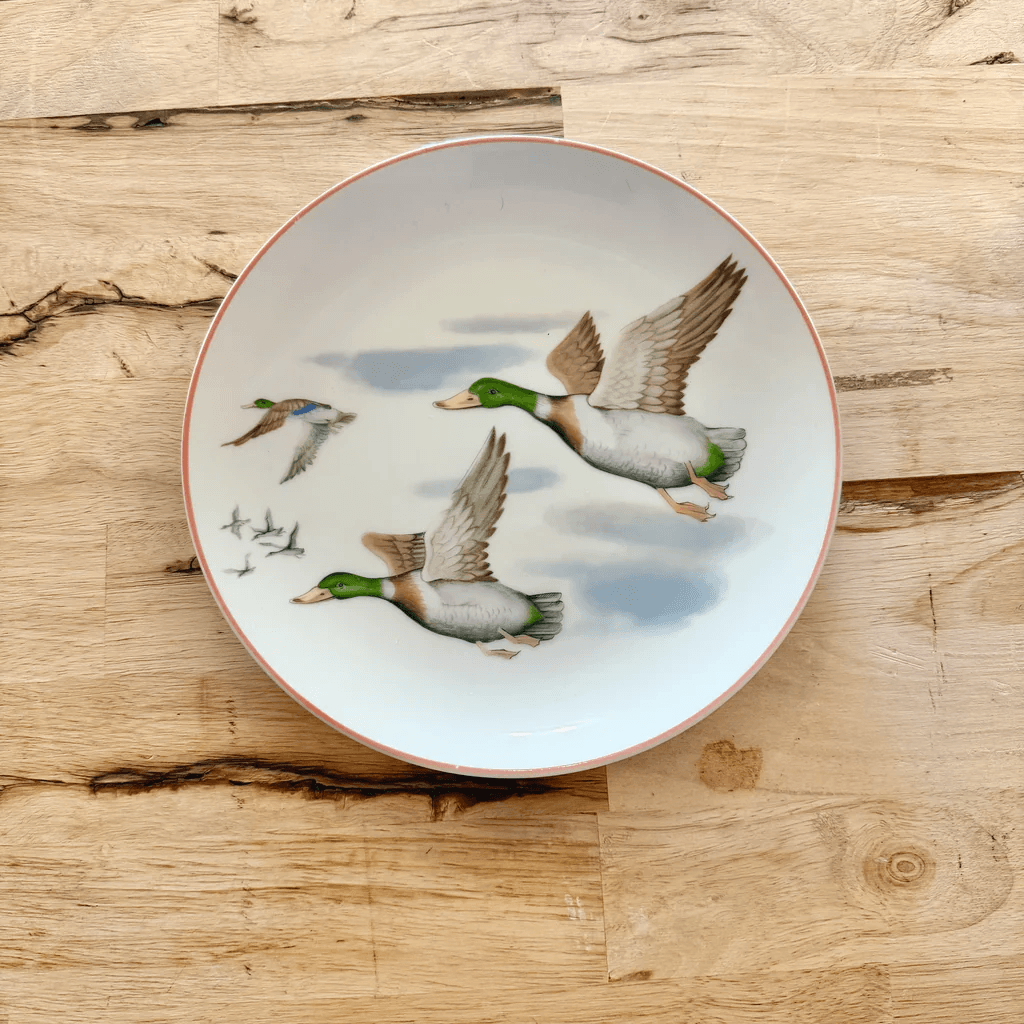20 Nashville FINDS for June: Father's Day Gifts, Chic Accessories & More - 19 A white ceramic plate with a painted design of three mallard ducks flying against a cloudy sky, placed on a wooden surface—an elegant Nashville FINDS piece perfect for your May table setting.