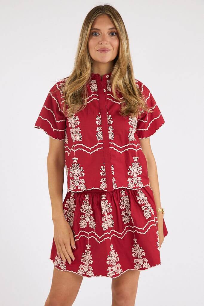 A woman stands against a plain background wearing a red short-sleeve top and matching skirt with white embroidered patterns—a perfect May look among Nashville finds.