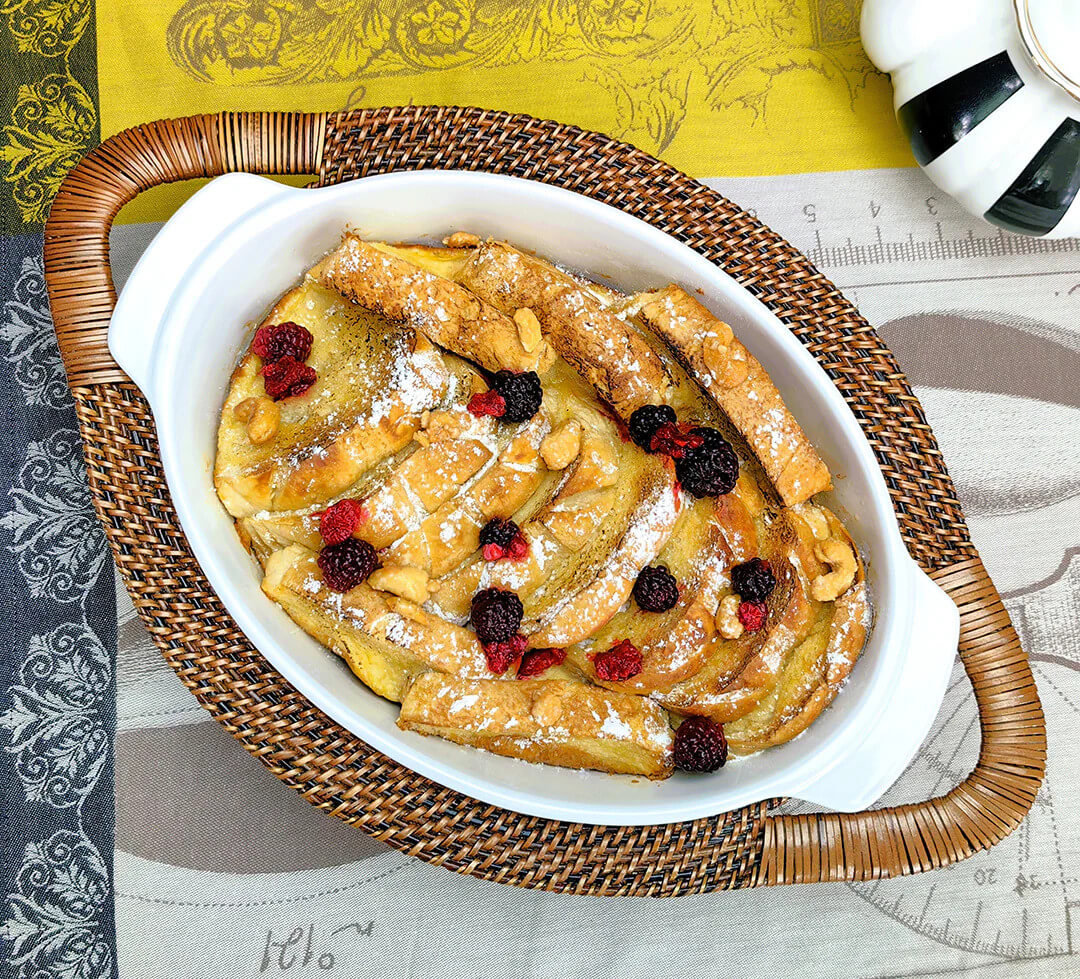 20 Nashville FINDS for June: Father's Day Gifts, Chic Accessories & More - 17 Oval dish containing a baked French toast casserole topped with powdered sugar, berries, and walnuts, spotted among May Nashville finds on a patterned tablecloth next to a striped teapot.