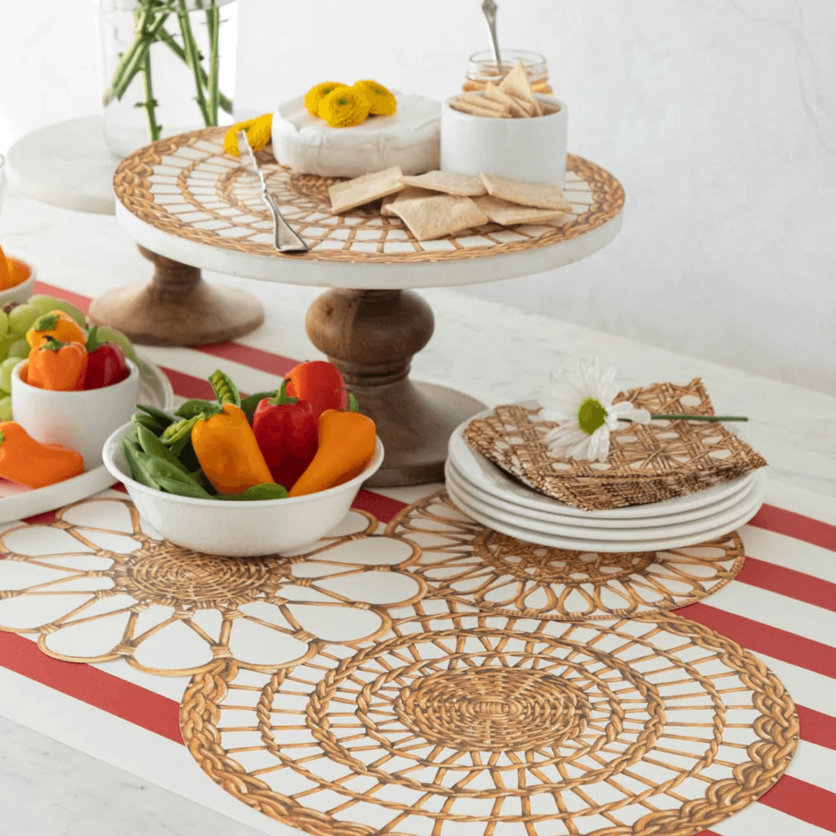 20 Nashville FINDS for June: Father's Day Gifts, Chic Accessories & More - 14 A table set for May in Nashville with woven placemats, a FINDS cake stand topped with cheese and crackers, colorful peppers, stacked white plates, wicker coasters, and a daisy flower.