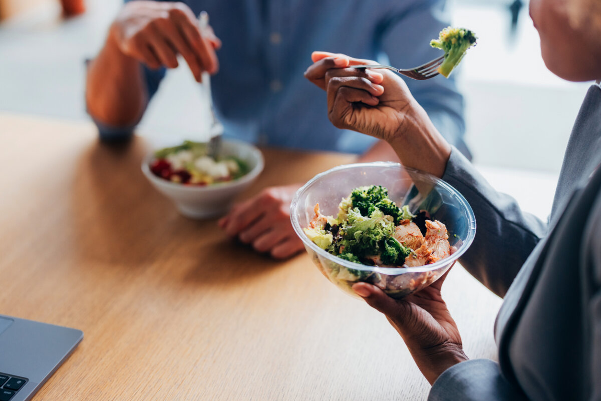 You Don't Need a Cleanse ... You Need More Fiber. - 3 Two people sit at a table enjoying high-fiber recipes, each eating salads from bowls, with one person holding a fork with broccoli close to their mouth.