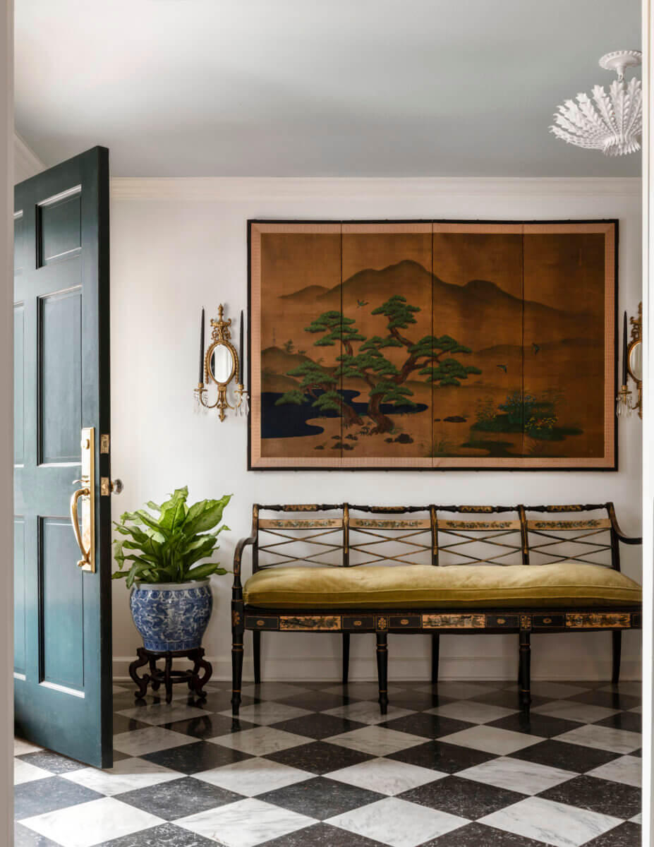 A bench sits on a black-and-white-tiled floor in an entryway. Sconces and framed art hang above it.