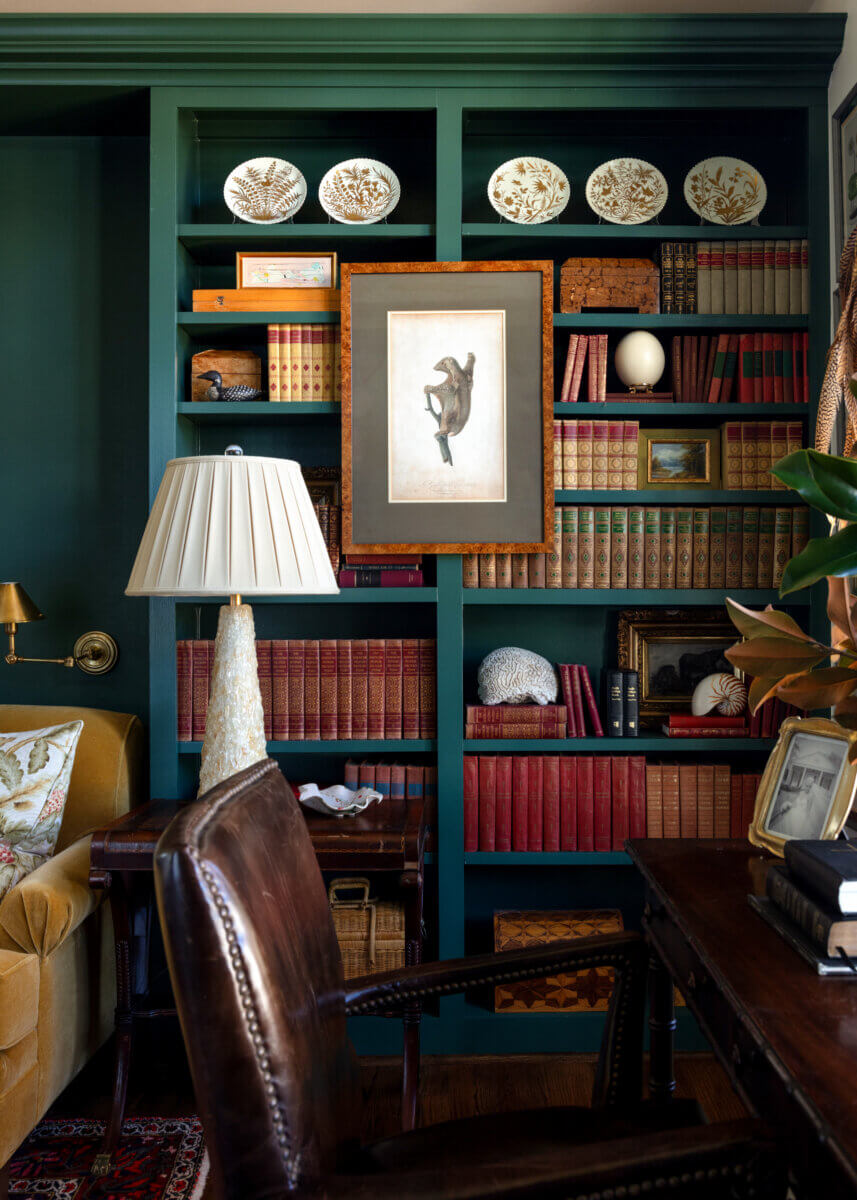 Interior of a home library in dark green, with a desk and leather chair.