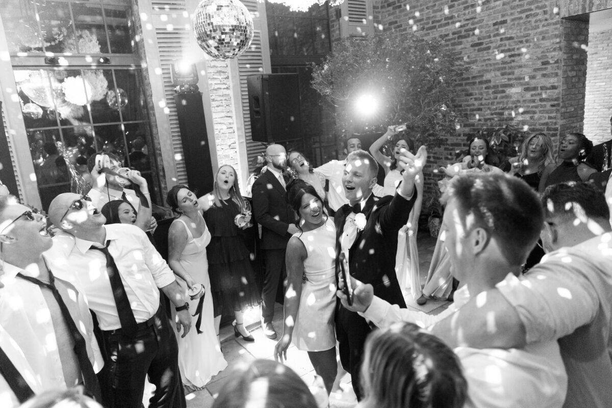 Disco Balls and Black-Tie Style Defined This Lexington Wedding - 12 A group of people dance and celebrate at an indoor event under a disco ball, with light reflections scattered across the scene, as wedding vows are joyfully exchanged amid the festive atmosphere.