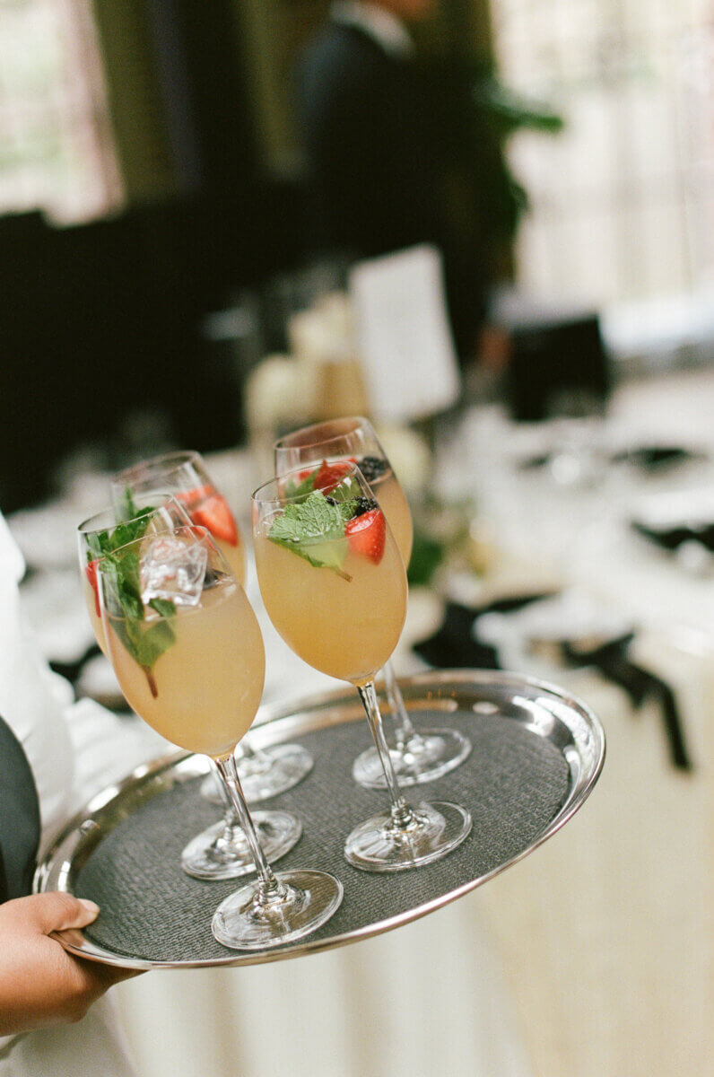 Disco Balls and Black-Tie Style Defined This Lexington Wedding - 8 A server holds a tray with four glasses of iced cocktails garnished with mint and fruit, set in a formal dining setting perfect for an elegant celebration.