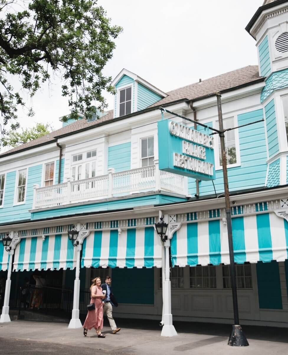 Savoring Louisiana: A Culinary Roadshow Across the State - 10 Two people walk past the iconic blue and white Commander's Palace Restaurant in Louisiana, its striped awnings hinting at a true Culinary experience.